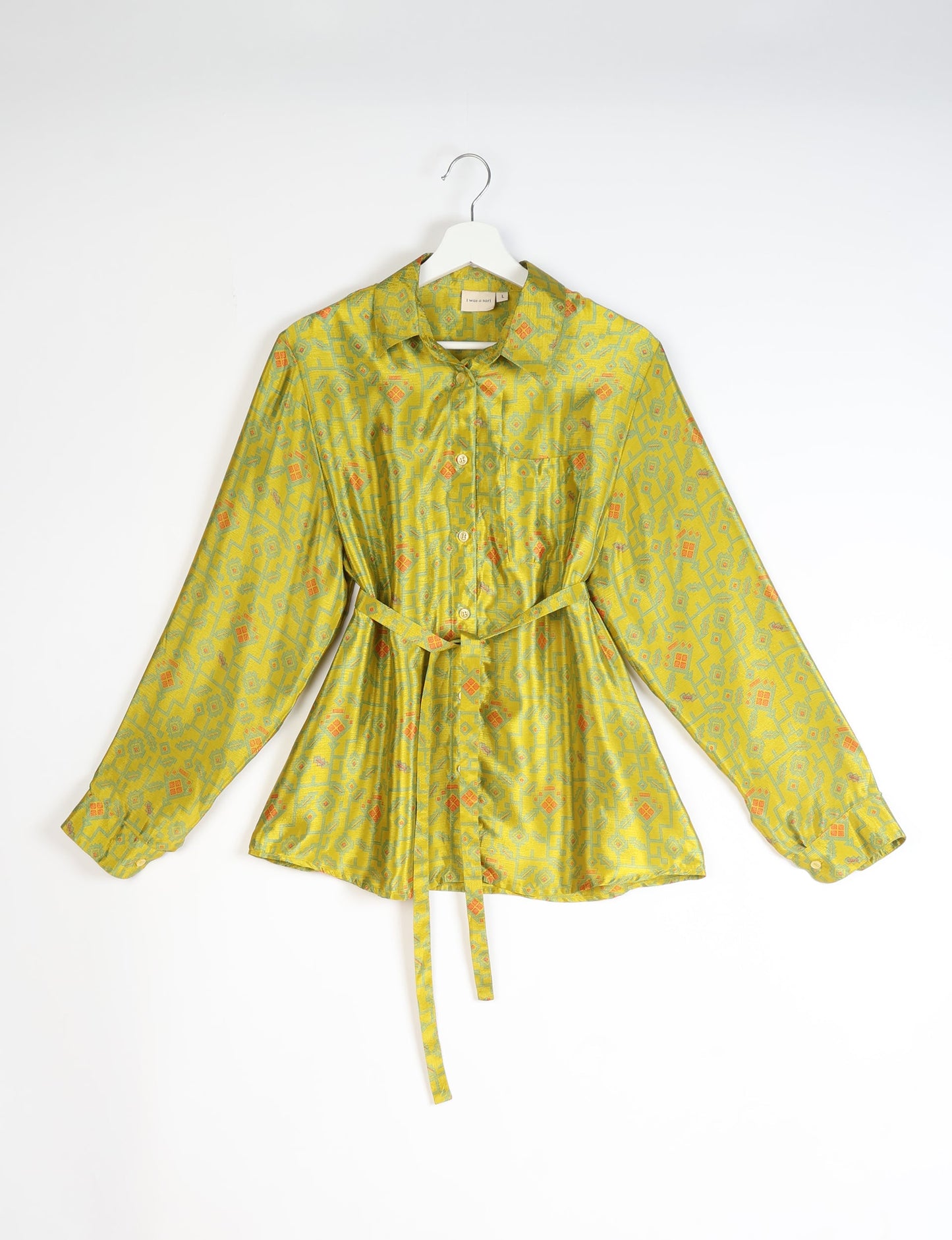 Yellow long-sleeve button-up shirt with abstract geometric pattern, collar, chest pocket, and waist tie, hanging on white hanger