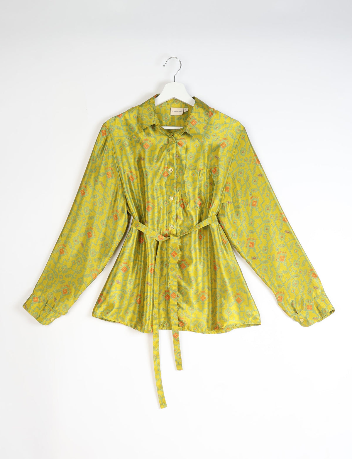 Yellow long-sleeve button-up shirt with abstract geometric pattern, collar, chest pocket, and waist tie, hanging on white hanger