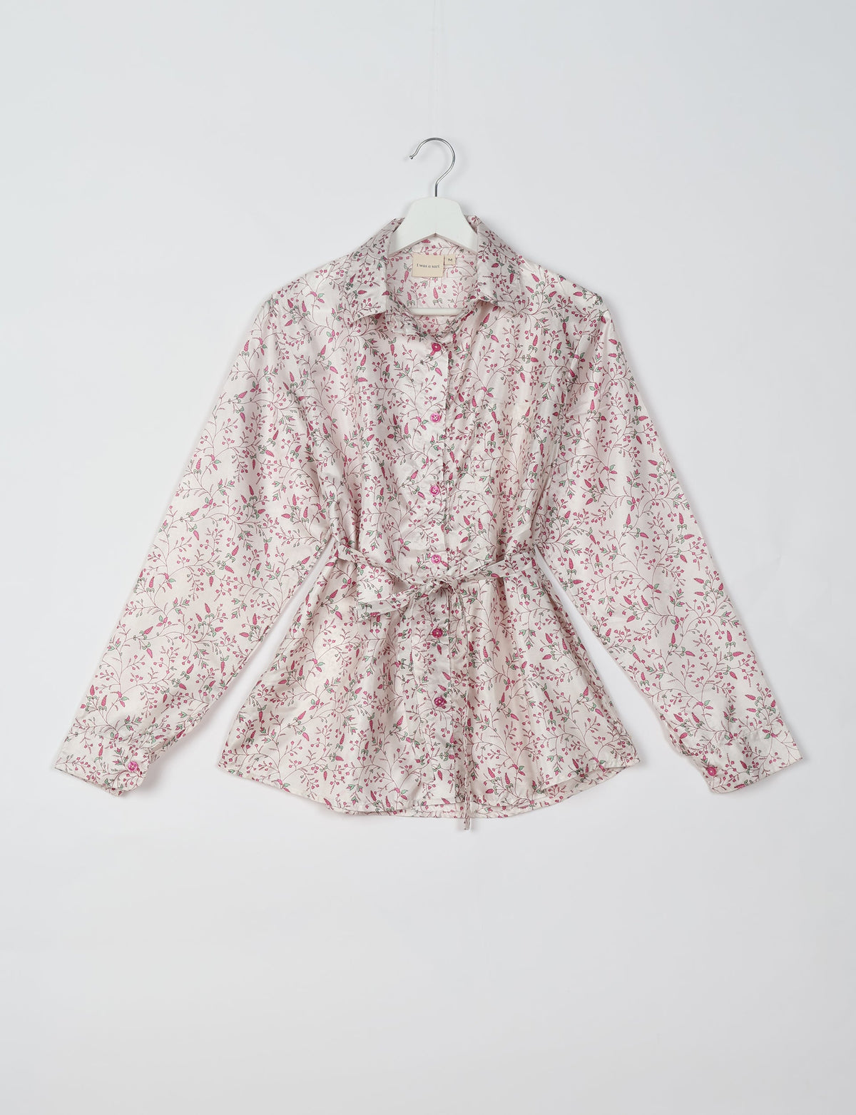 White button-up shirt with pink and green floral print, long sleeves, collar, and waist tie, hanging on white hanger