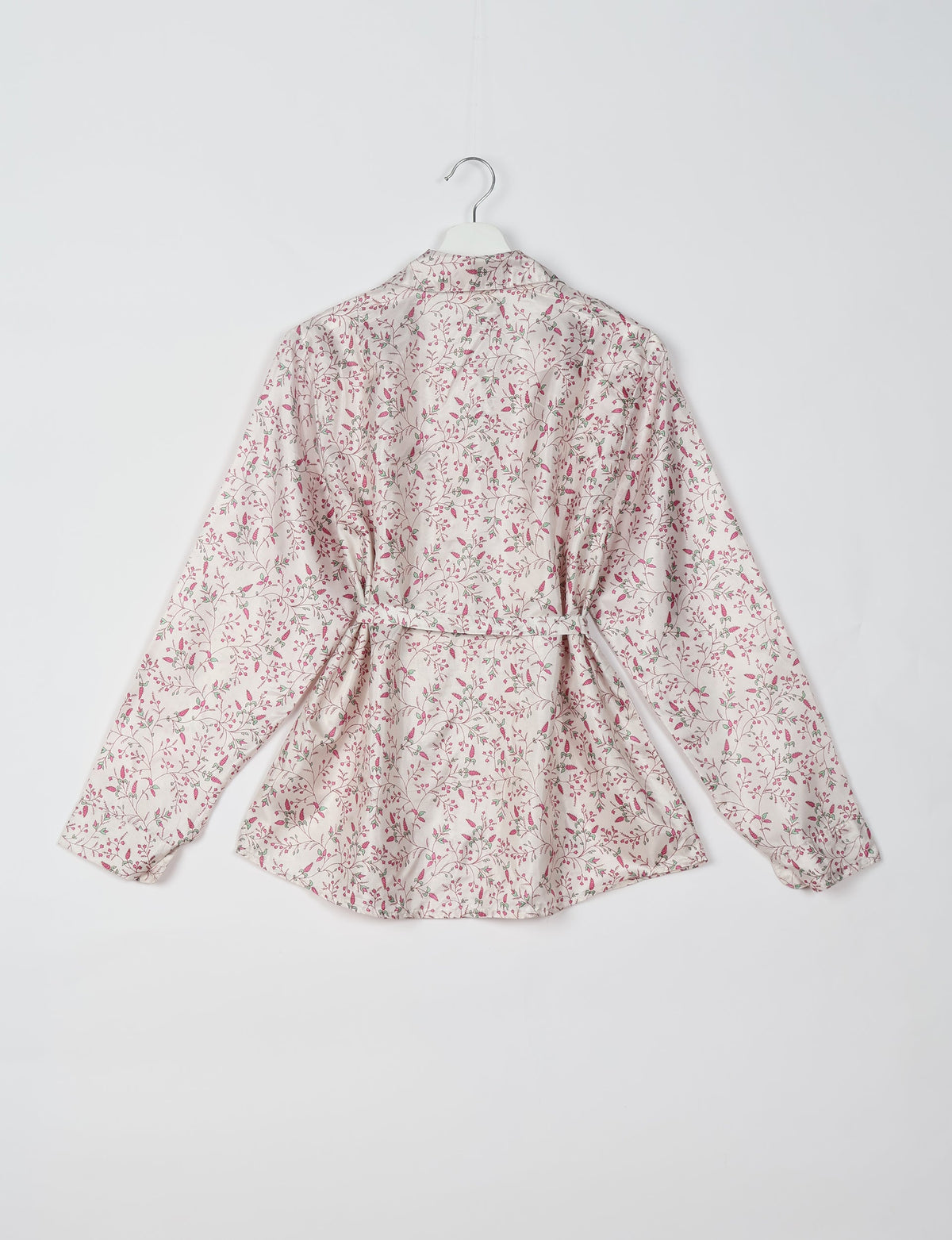 White long-sleeve shirt with pink and green floral vine pattern, belt at waist, shown from back on hanger