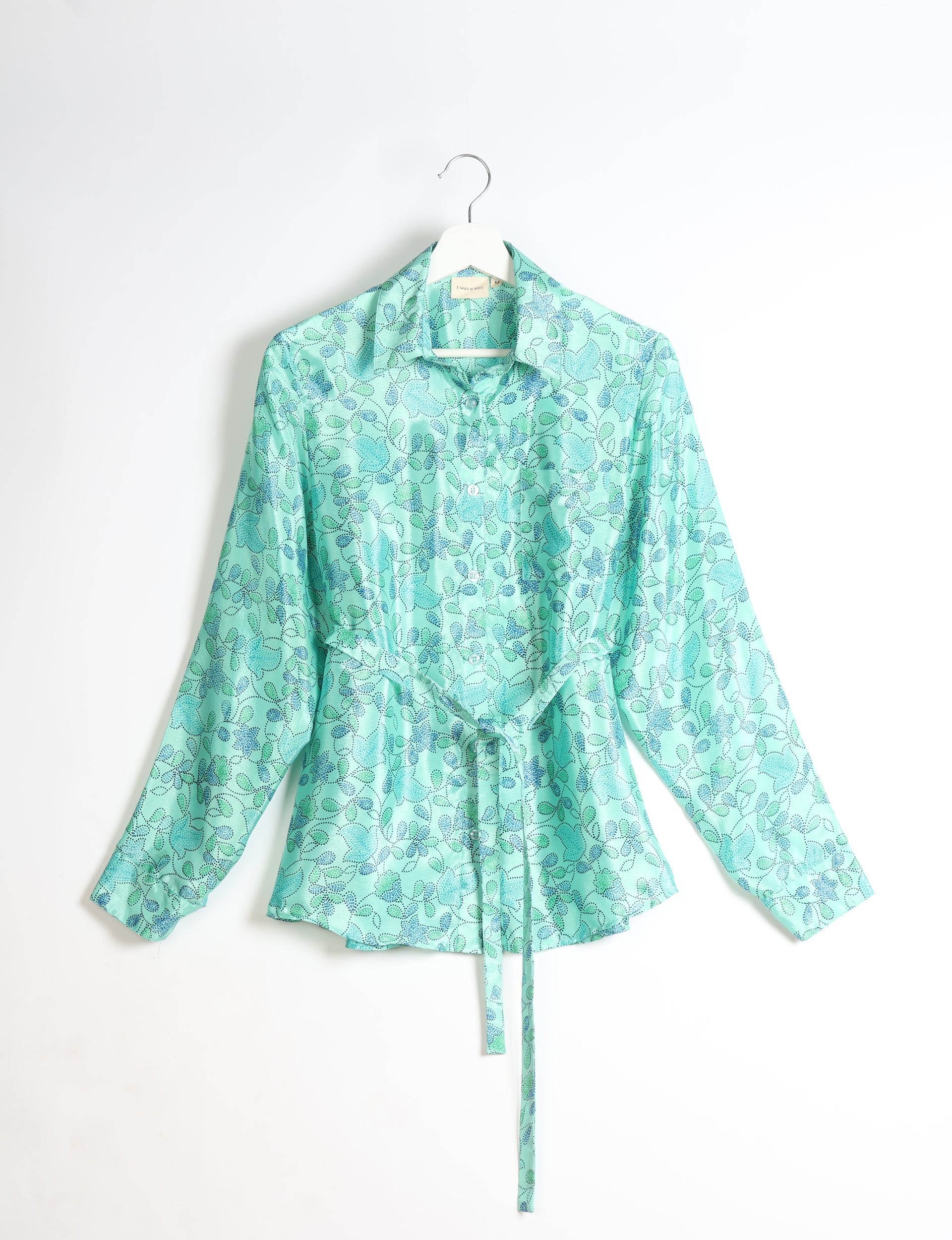 Green long-sleeve button-up shirt with blue and dark green floral pattern, collar, and waist tie, hanging on white hanger