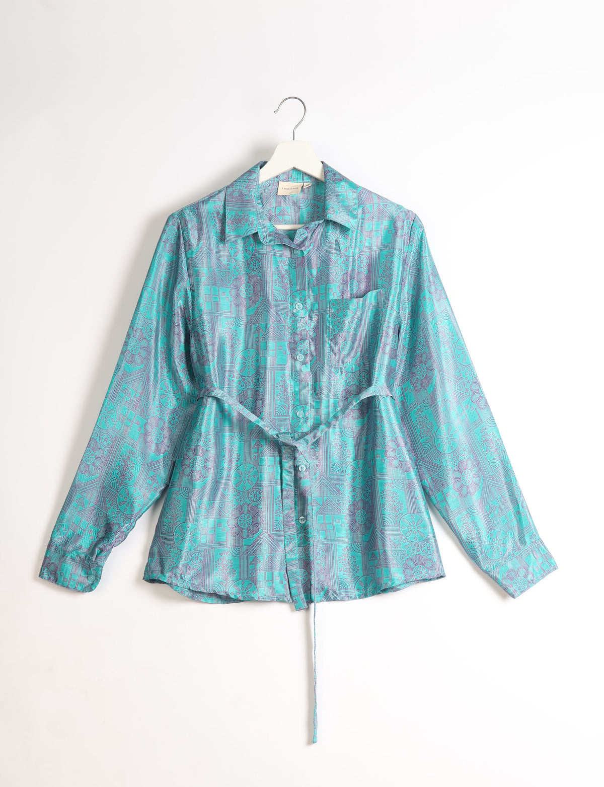 Blue button-up shirt with long sleeves, collar, chest pocket, belt tie, and geometric floral pattern hanging on white hanger