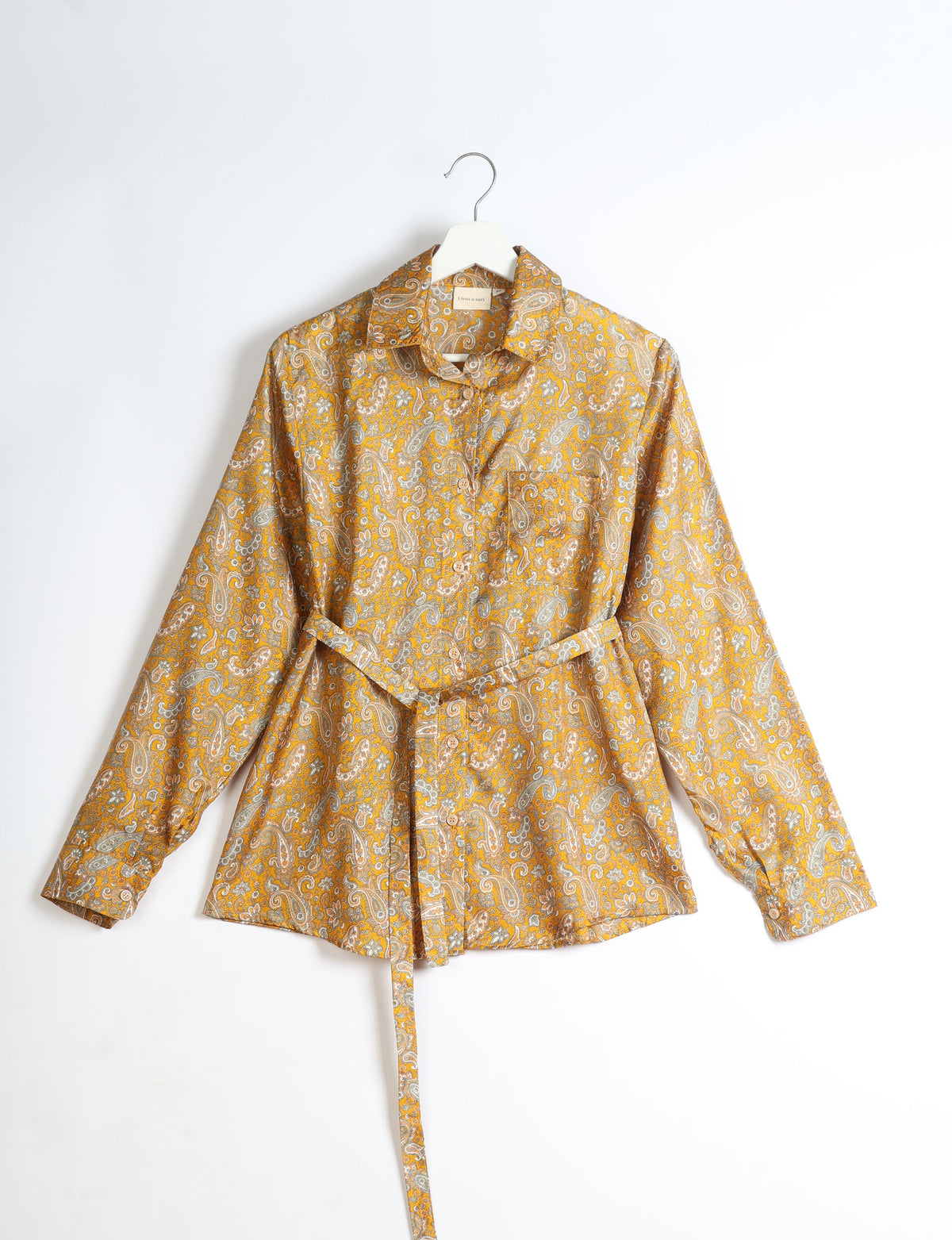 Yellow paisley long-sleeve shirt with collar, buttons, chest pocket, and matching fabric belt, hanging on white hanger