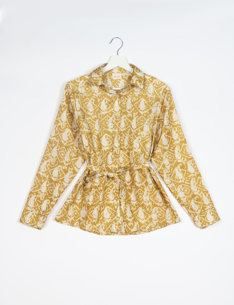 Long-sleeve button-up shirt with collar and belt, mustard yellow with white abstract tropical print, hanging on white hanger