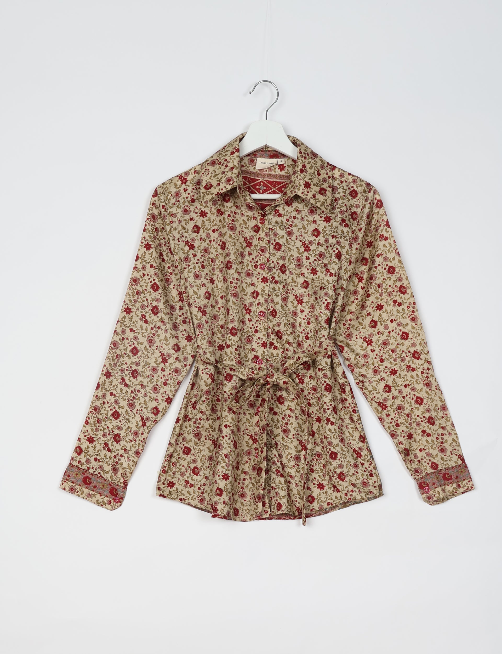 Beige long-sleeve button-up shirt with red floral print, collar, tie waist, and patterned cuffs hanging on white hanger