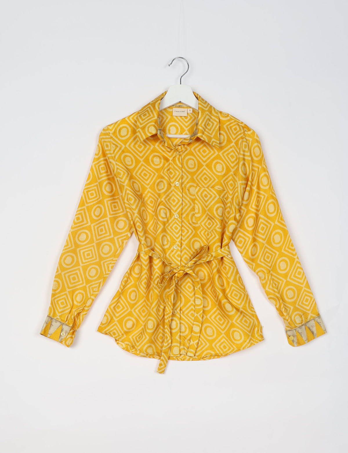 Yellow geometric patterned long-sleeve shirt with collar, front buttons, chest pocket, and waist tie, shown on hanger