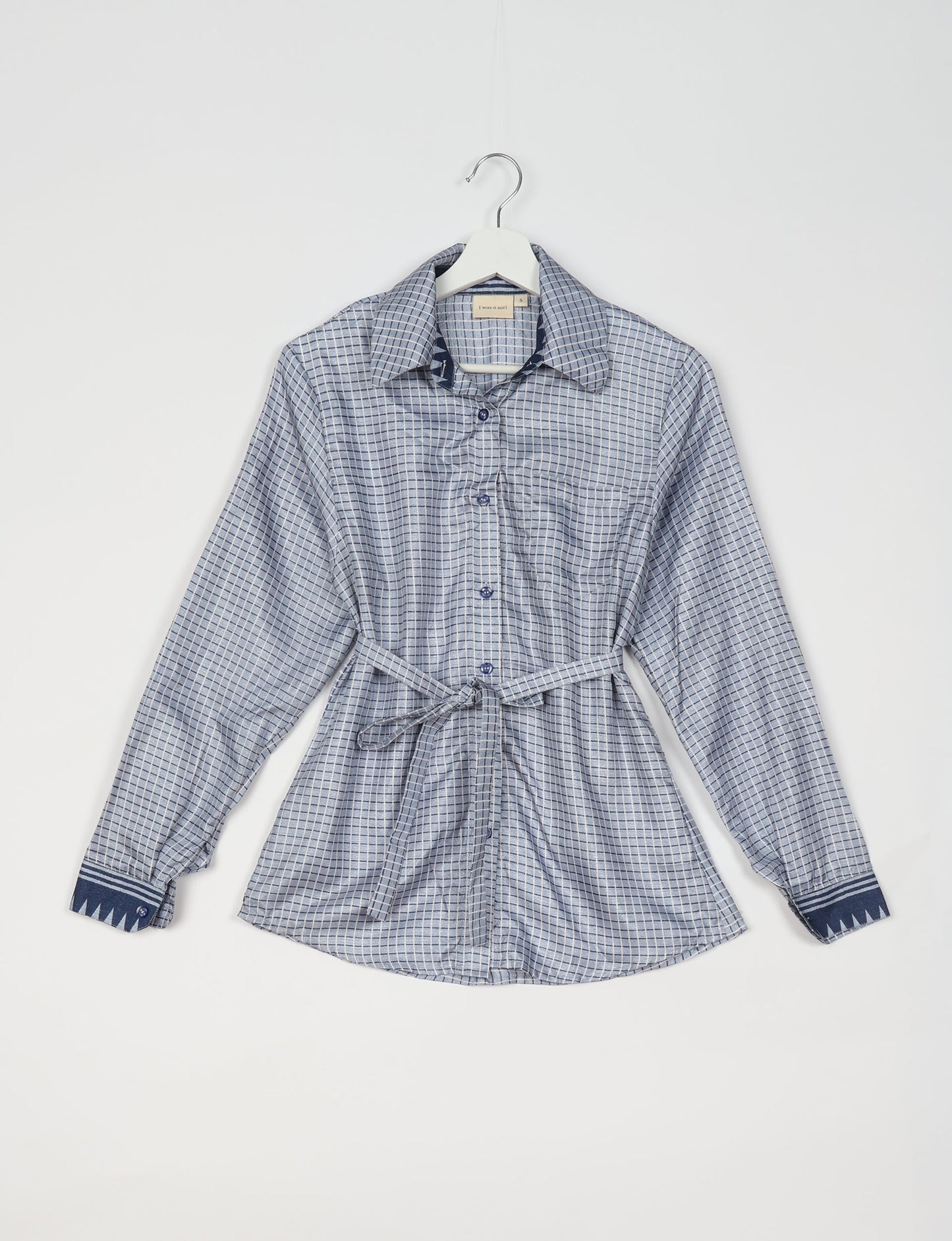 Experience sustainable fashion with our classic slim-fit shirt, crafted with ethical and green values. The shirt, designed for minimal waste, features a tie-up waist belt or neck tie, semi-spread collar, and regular shirt cuffs. Versatile and eco-friendly, wear it tucked in, unbuttoned over a tank top, or knotted at the waist for a unique style.