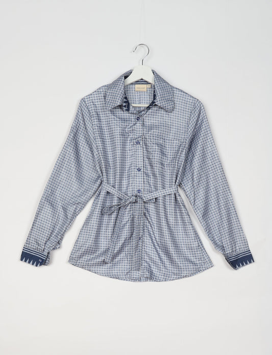 Experience sustainable fashion with our classic slim-fit shirt, crafted with ethical and green values. The shirt, designed for minimal waste, features a tie-up waist belt or neck tie, semi-spread collar, and regular shirt cuffs. Versatile and eco-friendly, wear it tucked in, unbuttoned over a tank top, or knotted at the waist for a unique style.