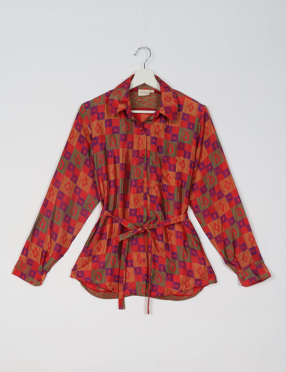 Red ethnic patterned long-sleeve shirt with collar, buttons, front pocket, and waist tie, hanging on a white hanger