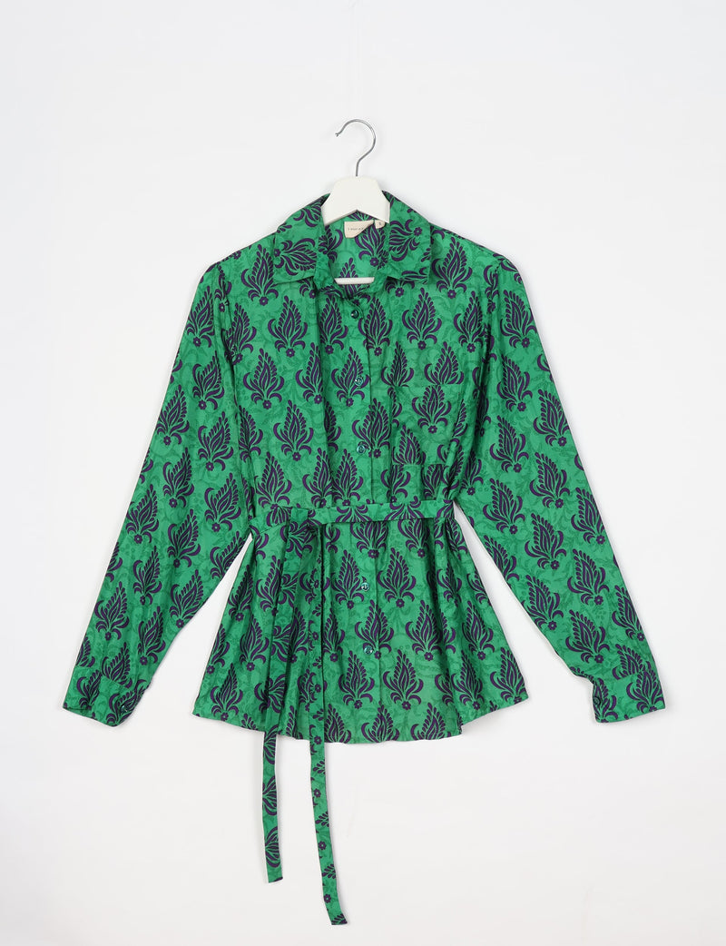 Green long-sleeve button-up shirt with dark leaf and floral pattern, collar, chest pocket, and waist tie, hanging on white hanger
