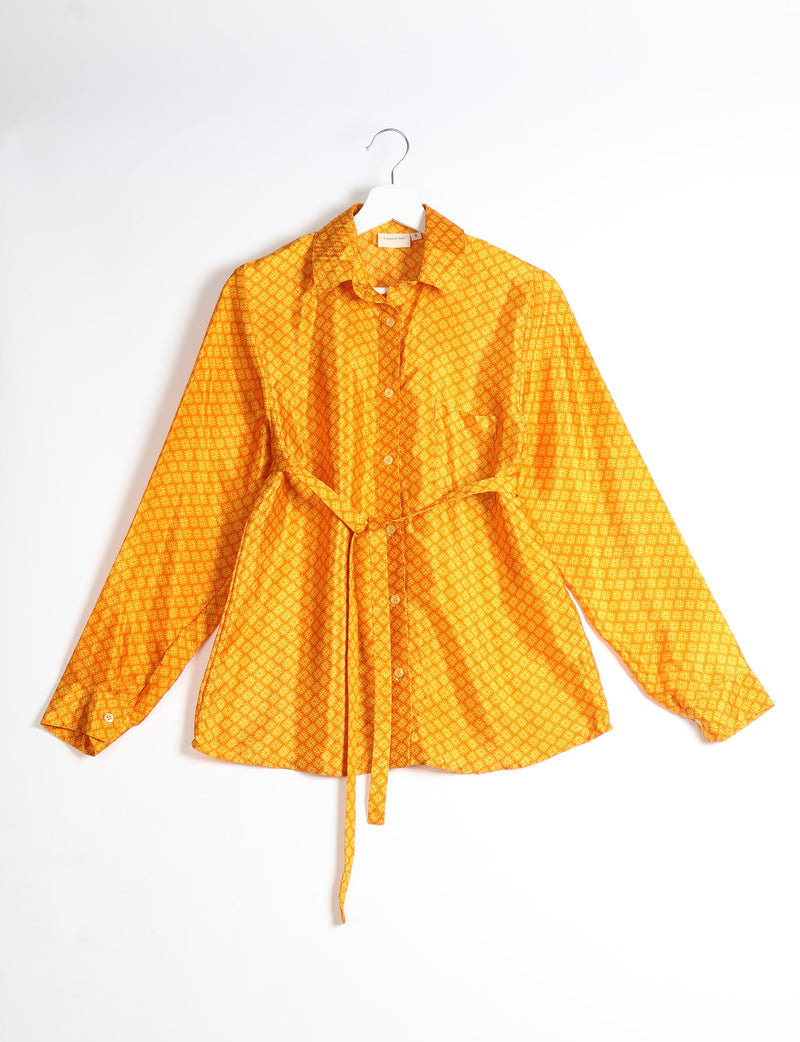 Yellow button-up shirt with micro geometric pattern, long sleeves, collar, front pocket, and waist tie, hanging on white