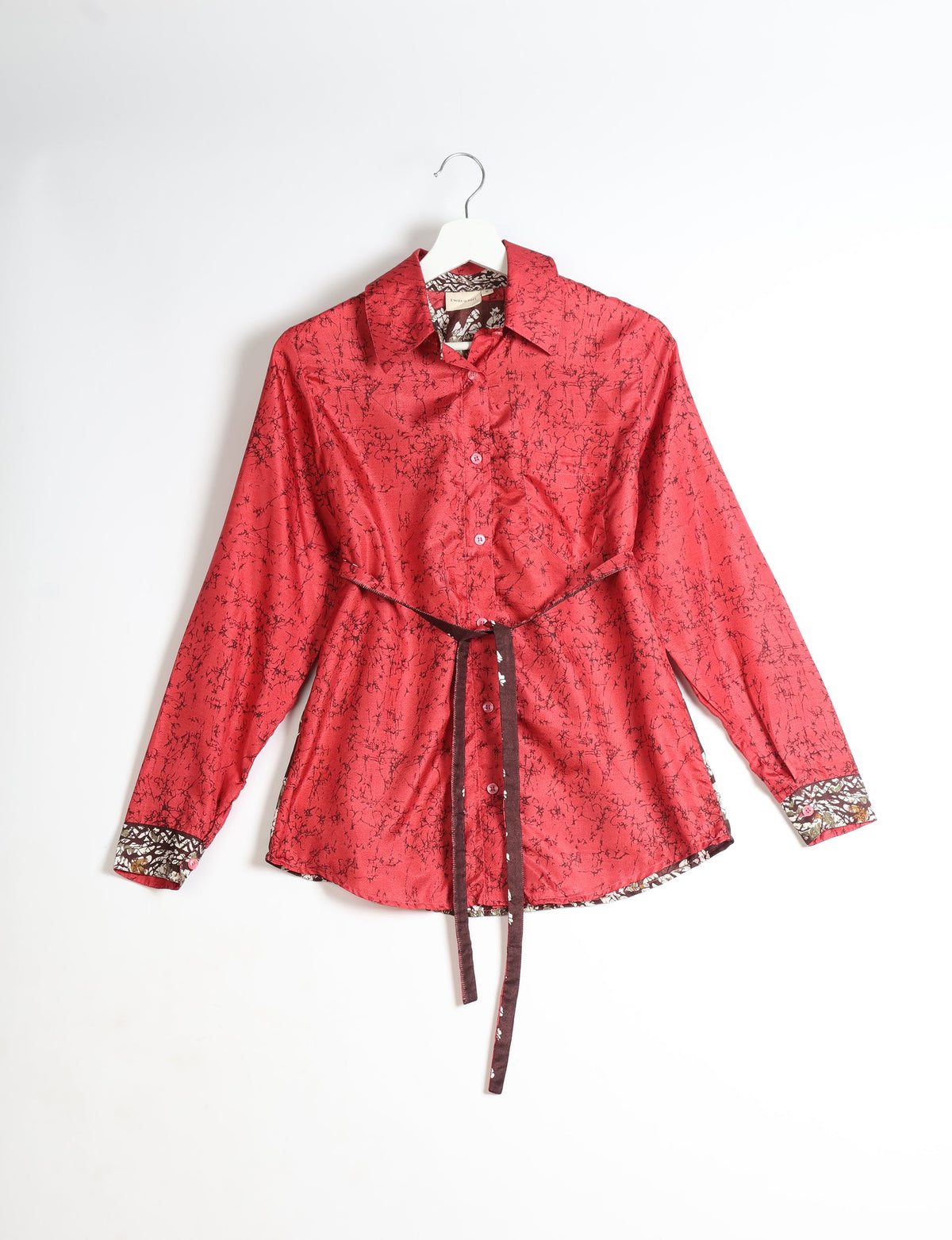 Red long-sleeve button-up shirt with black abstract pattern, floral inner collar and cuffs, and brown waist tie, on hanger