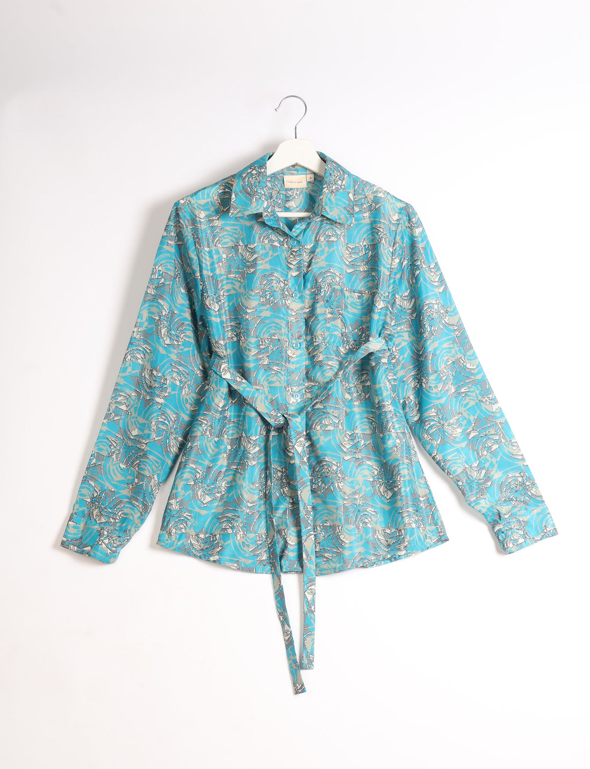 Blue long-sleeve button-up shirt with abstract white and gray floral pattern, collar, and waist tie, hanging on white hanger