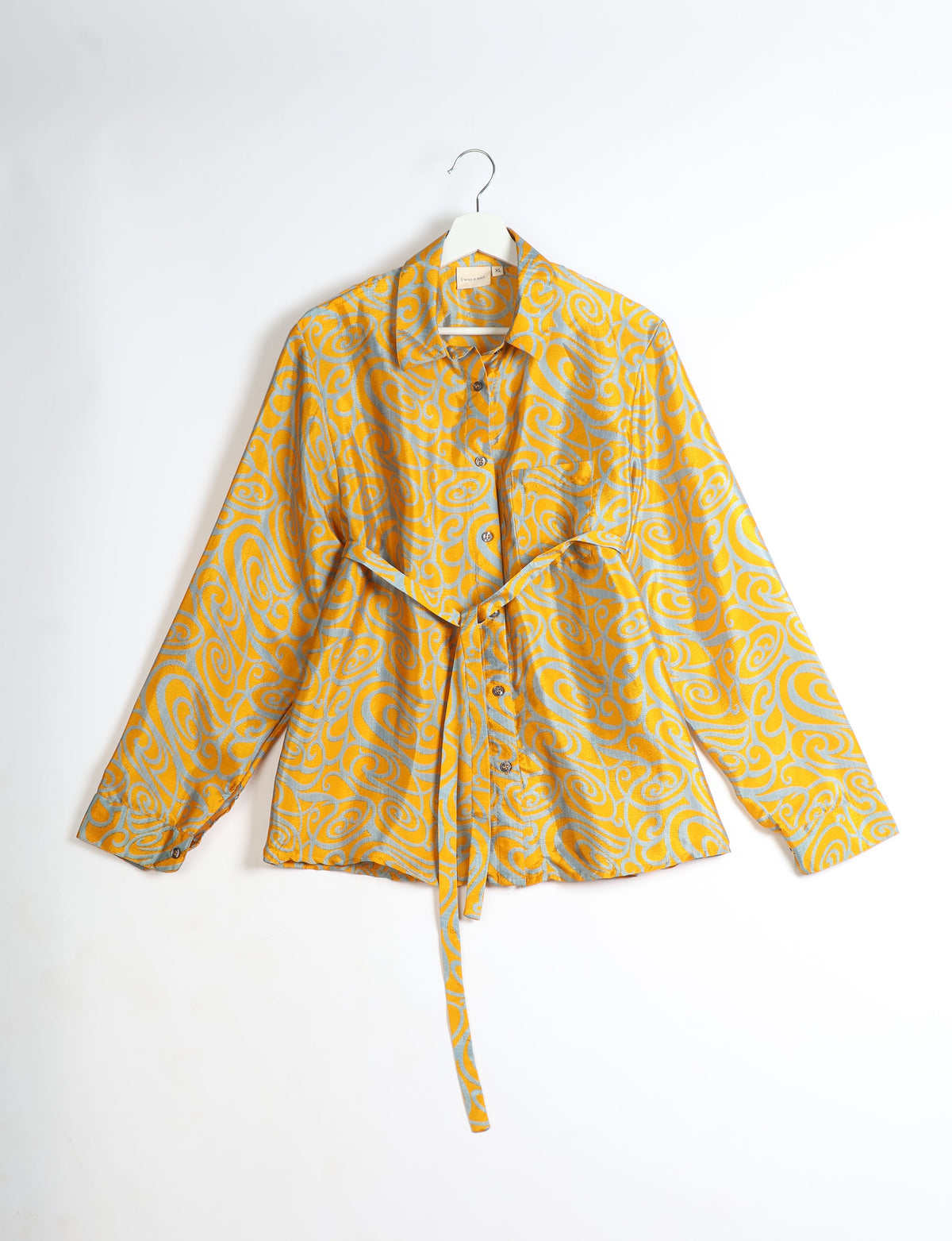 Yellow shirt with abstract gray swirl pattern, button front, collar, long sleeves, and waist tie, hanging on white hanger