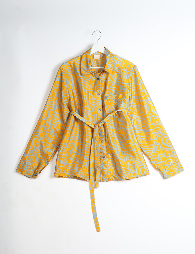 Yellow shirt with abstract gray swirl pattern, button front, collar, long sleeves, and waist tie, hanging on white hanger