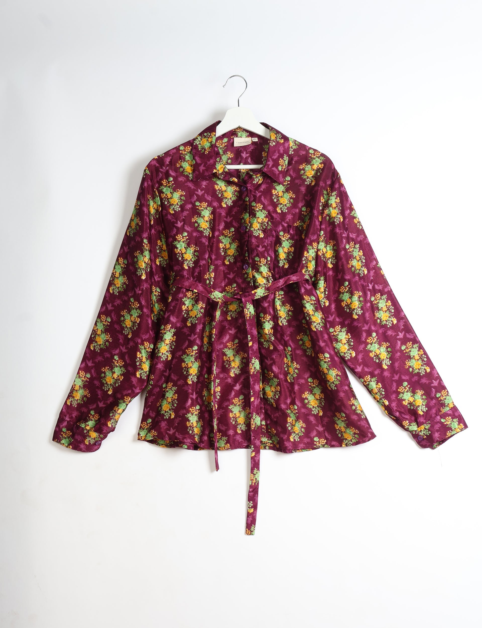 Purple long-sleeve button-up shirt with yellow and green floral print, collar, and waist tie, hanging on white hanger
