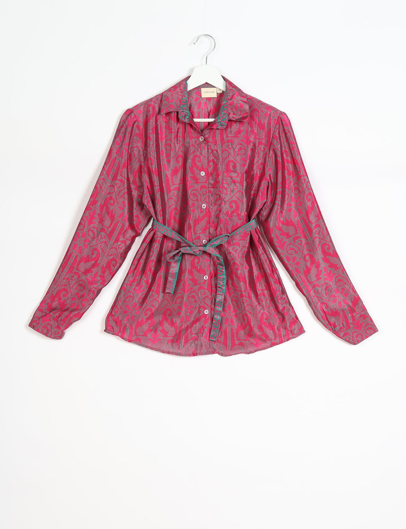 Pink long-sleeve button-up shirt with tropical floral pattern, green trim on collar and belt, hanging on white hanger