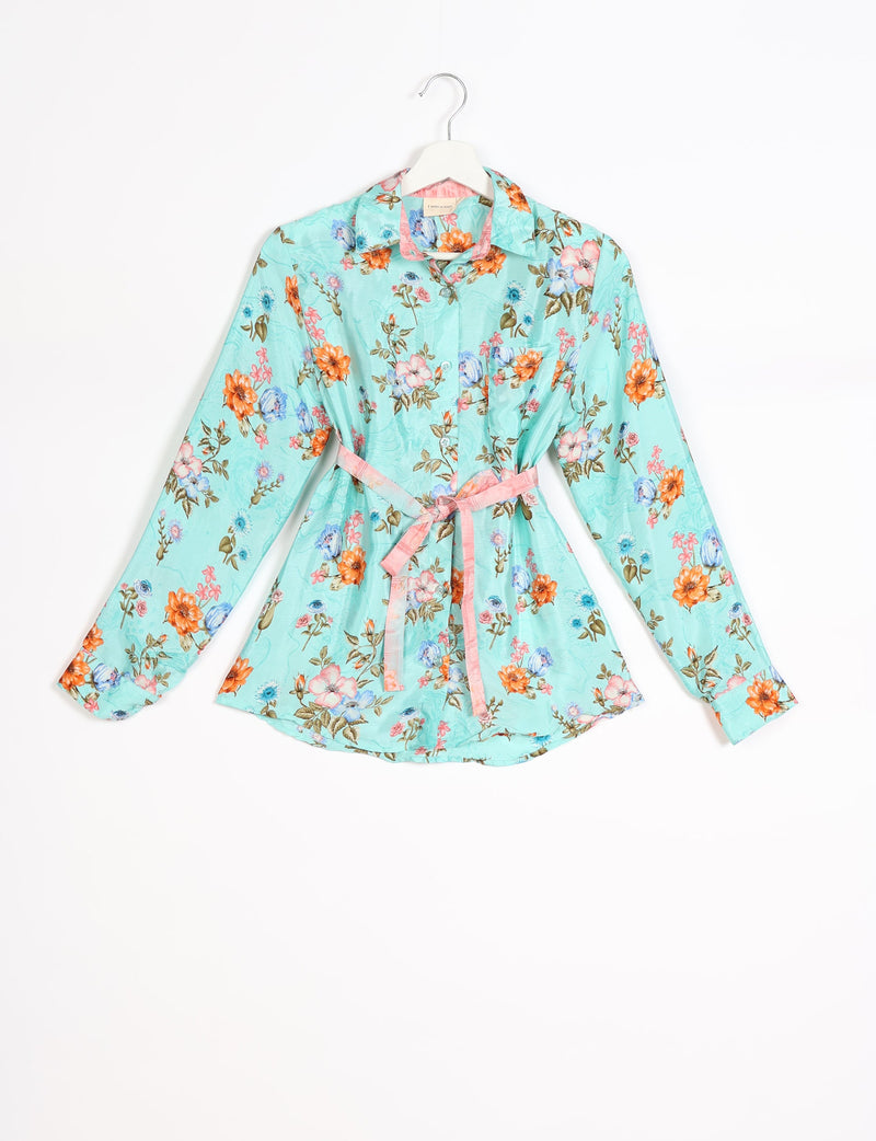 Light blue long-sleeve shirt with orange, pink, and blue floral print, pink belt, and front pocket, hanging on white hanger
