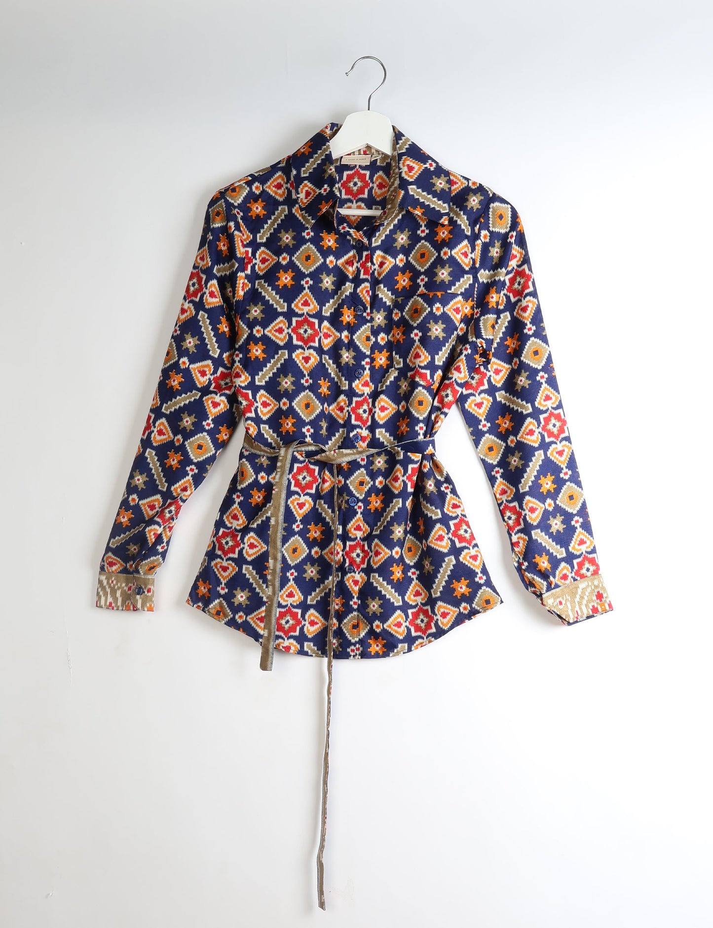Long-sleeve button-up shirt with geometric red, orange, beige, and white patterns on navy blue, hanging on white hanger