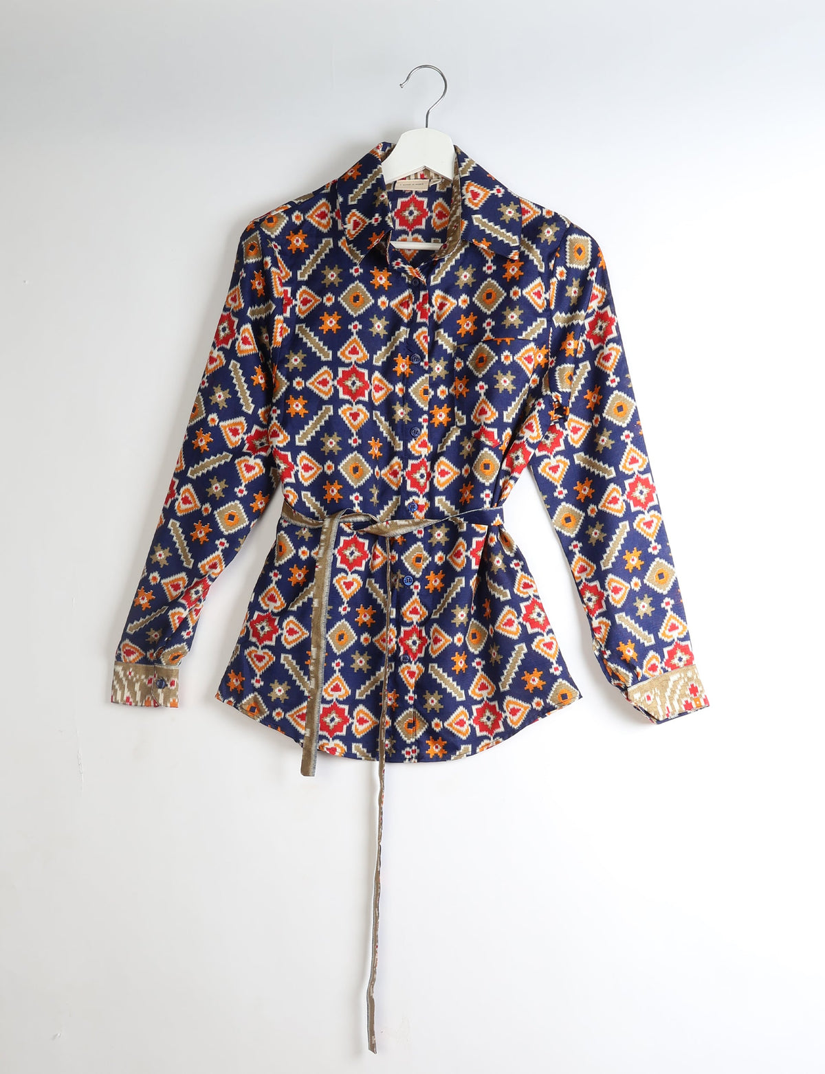 Long-sleeve button-up shirt with geometric red, orange, beige, and white patterns on navy blue, hanging on white hanger