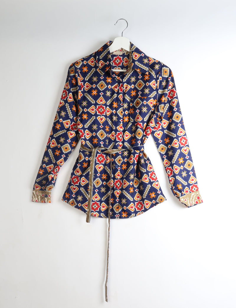 Long-sleeve button-up shirt with geometric red, orange, beige, and white patterns on navy blue, hanging on white hanger