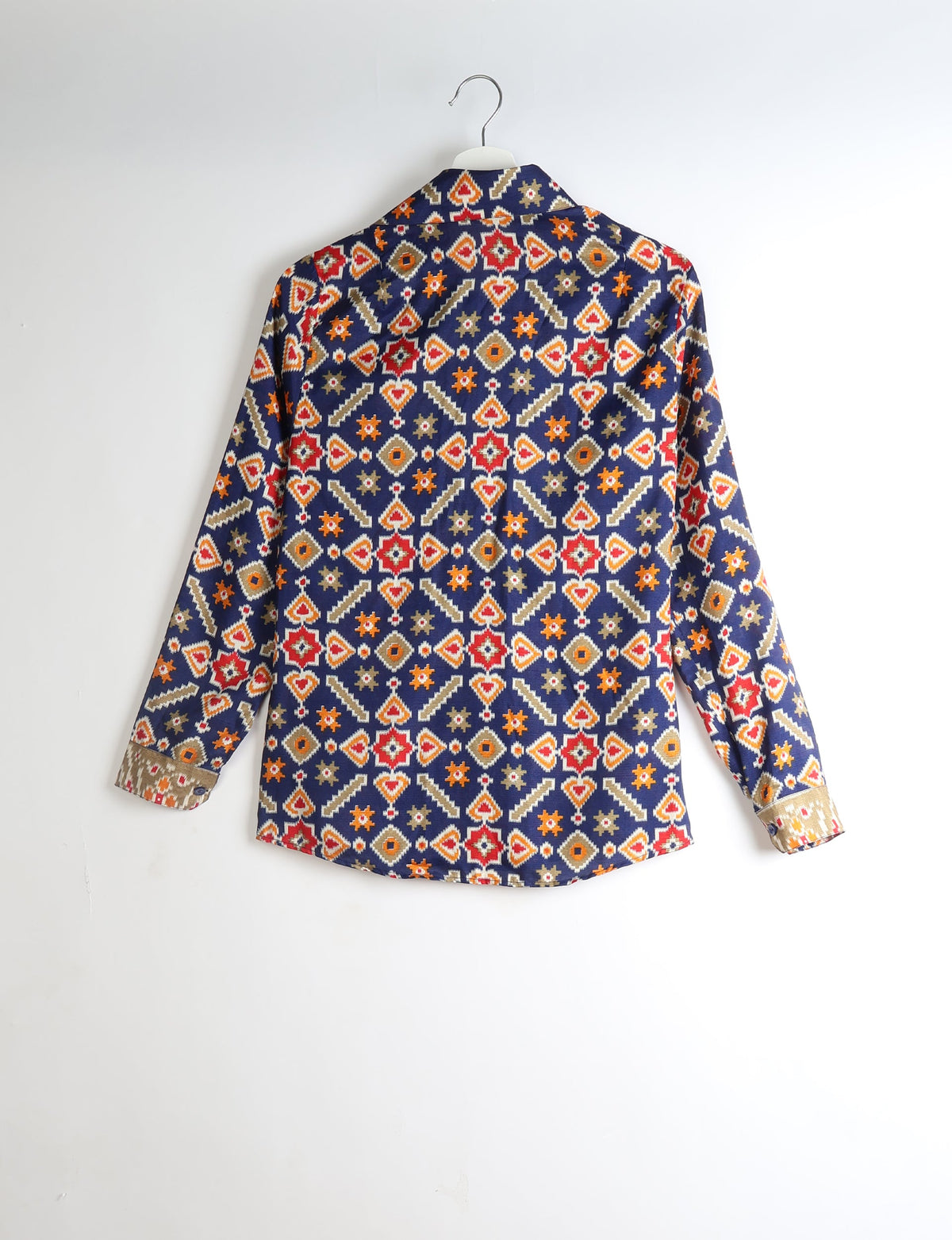 Long-sleeve shirt with navy blue base and geometric red, orange, beige, and white pattern, shown from back on hanger