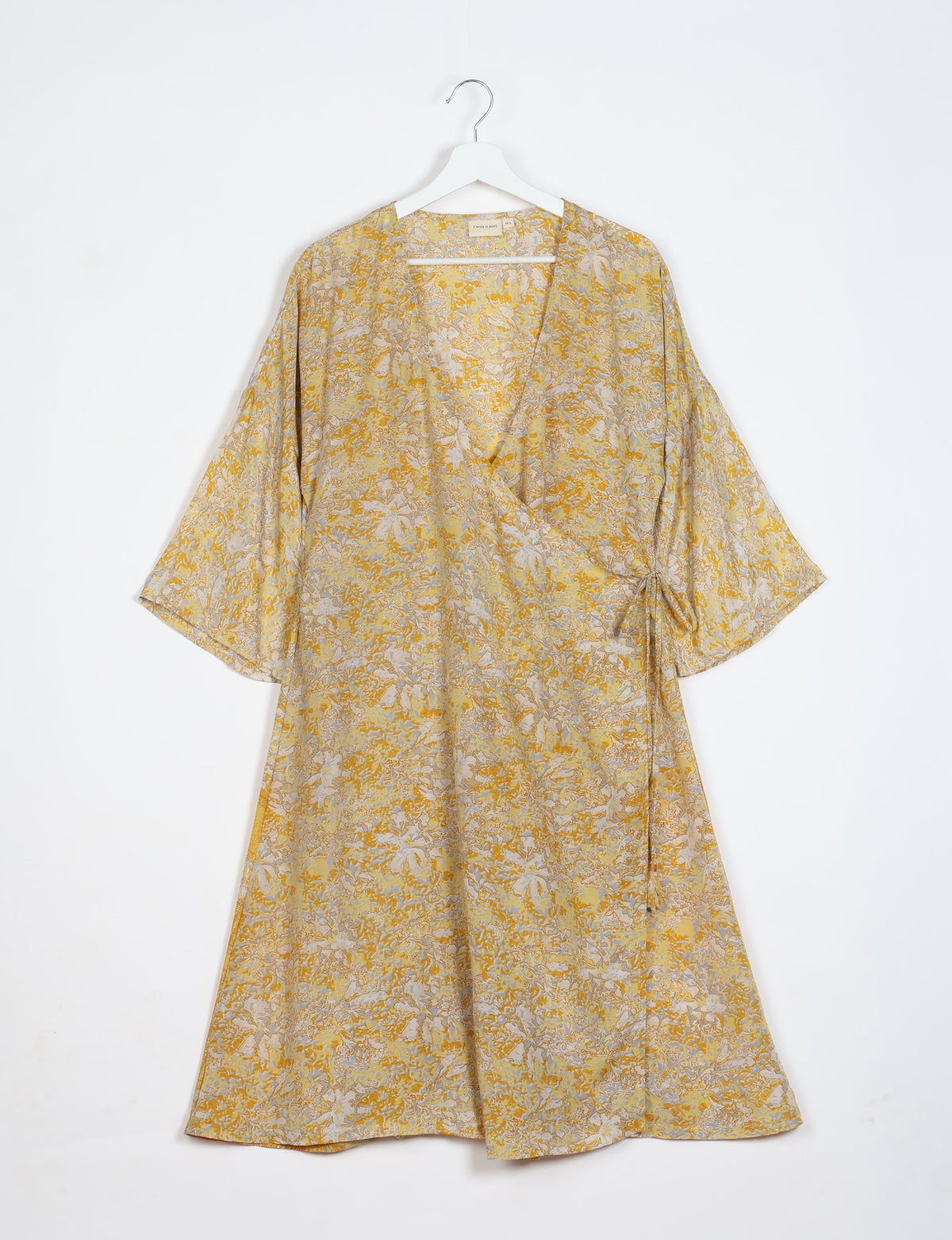 Yellow tropical floral wrap coat with wide sleeves hanging on white hanger against white background