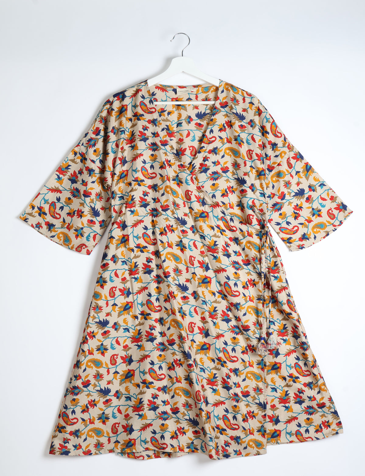 Beige wrap coat with colorful paisley and floral print, wide sleeves, and tassel tie belt, hanging on white hanger