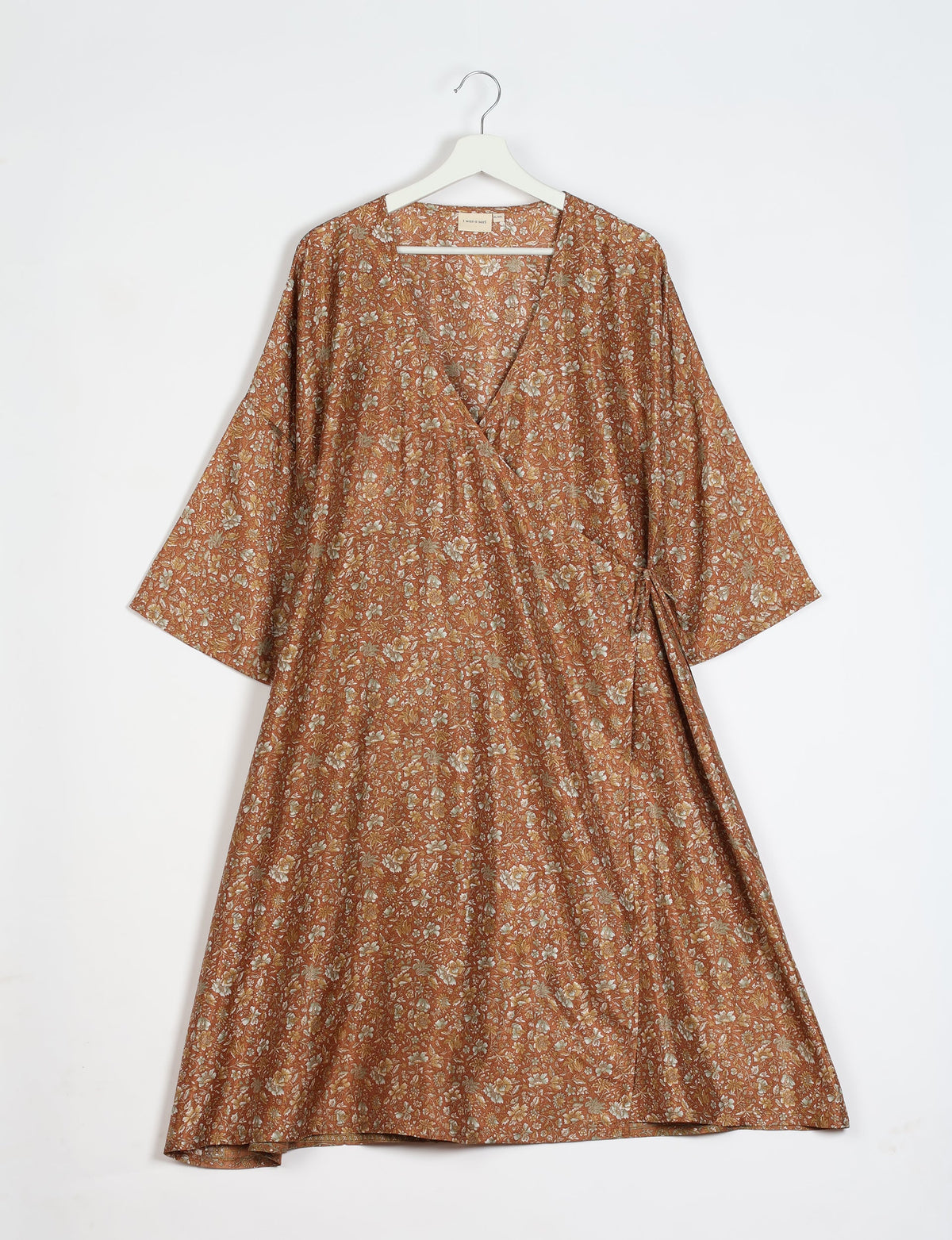 Brown tropical floral wrap coat with wide sleeves hanging on white hanger against white background