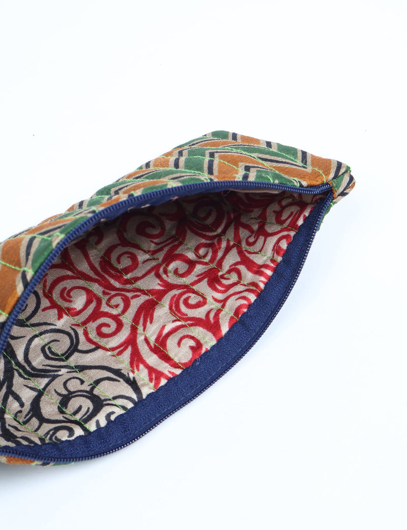 Quilted pencil pouch with blue zipper, green, orange, and black geometric exterior, and red swirl patterned interior lining
