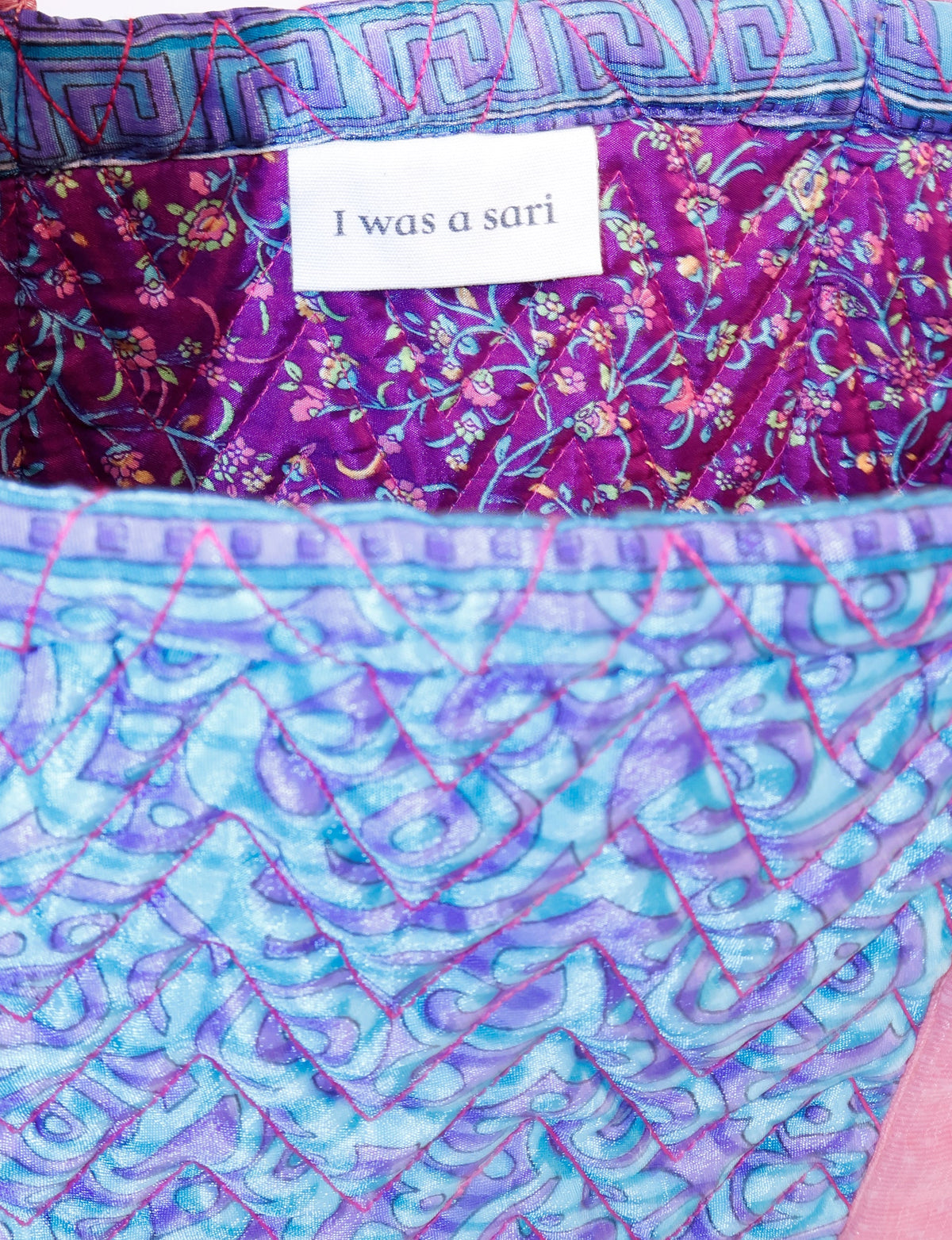 Quilted fabric with blue abstract pattern and purple floral interior lining with label reading "I was a sari"