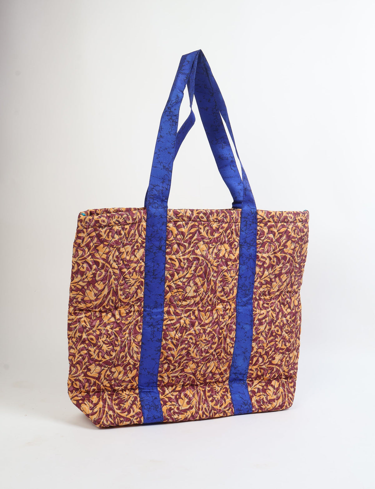 Quilted tote bag with red and yellow tropical leaf pattern and blue handles, shown front view standing upright