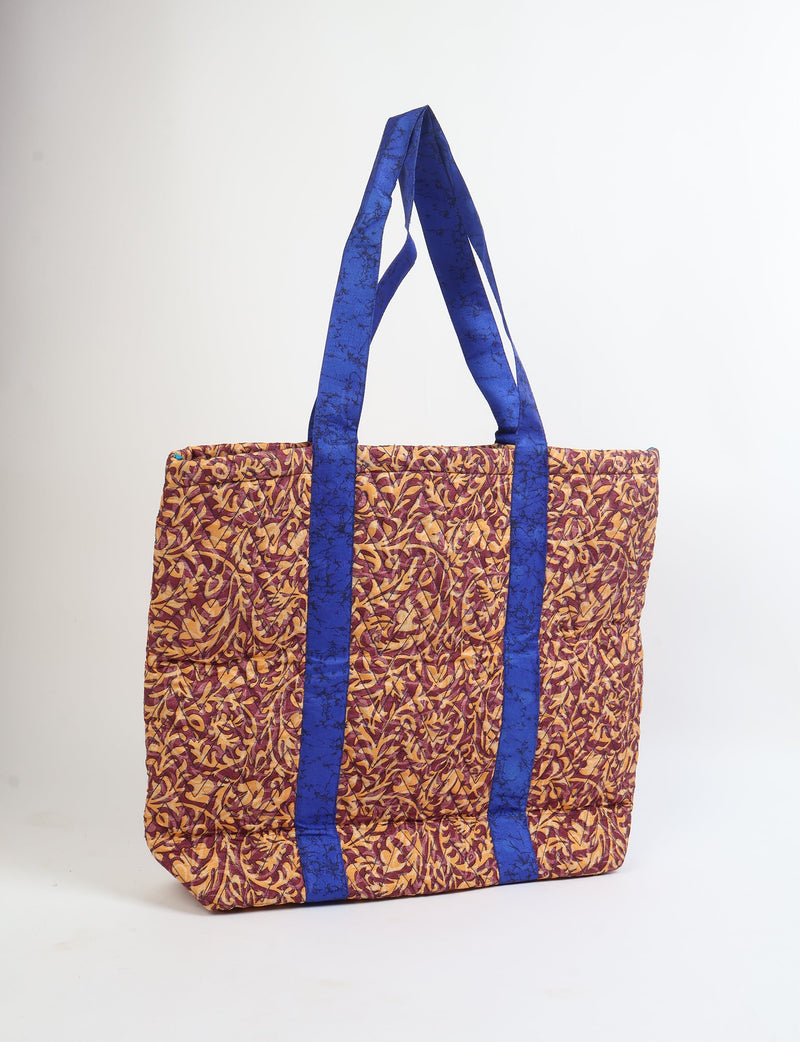 Quilted tote bag with red and yellow tropical leaf pattern and blue handles, shown front view standing upright