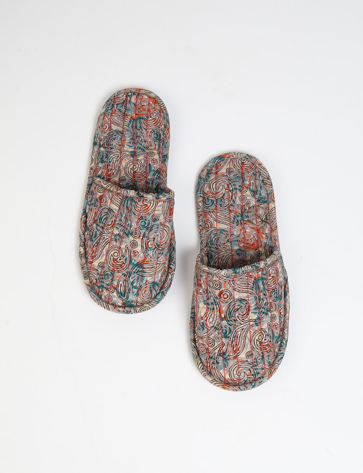 Pair of quilted slippers with beige paisley pattern in teal, orange, and black, shown from top view on white background