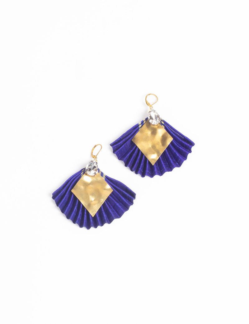 Pair of pleated earrings with blue fabric fans, hammered gold diamond shapes, and clear teardrop crystals, flat lay view