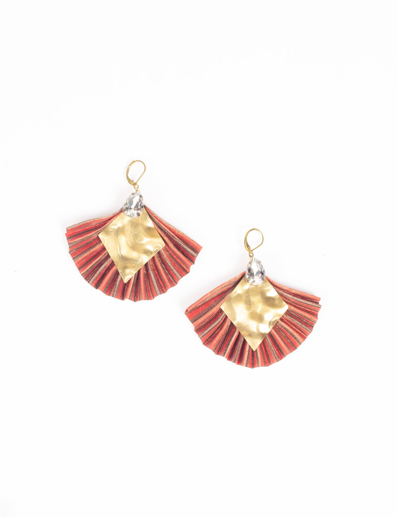 Pair of pleated earrings with orange and red striped fabric, hammered gold diamond shapes, and clear teardrop crystals, flat lay