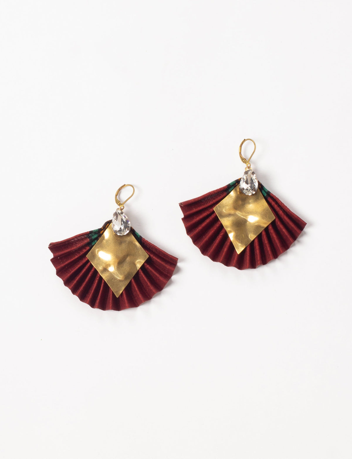 Pair of pleated earrings with red fabric fans, gold diamond-shaped metal pieces, and clear teardrop crystals, flat lay view