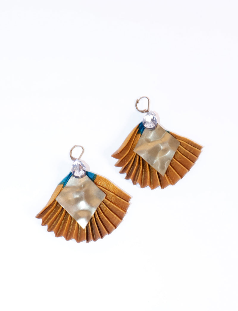 Pleated earrings with orange fabric, hammered gold-tone metal square, clear teardrop gem, and lever-back hooks, flat lay