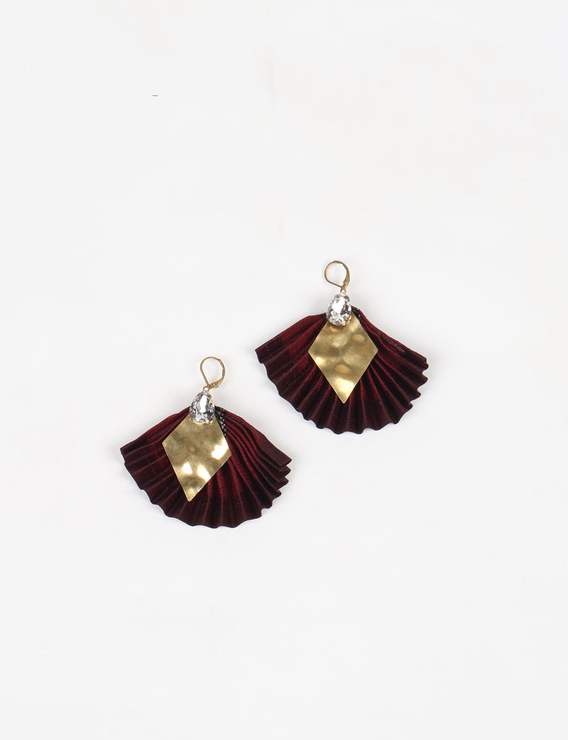Pair of pleated earrings with deep red fabric, gold diamond-shaped metal accents, and clear teardrop crystals, flat lay view