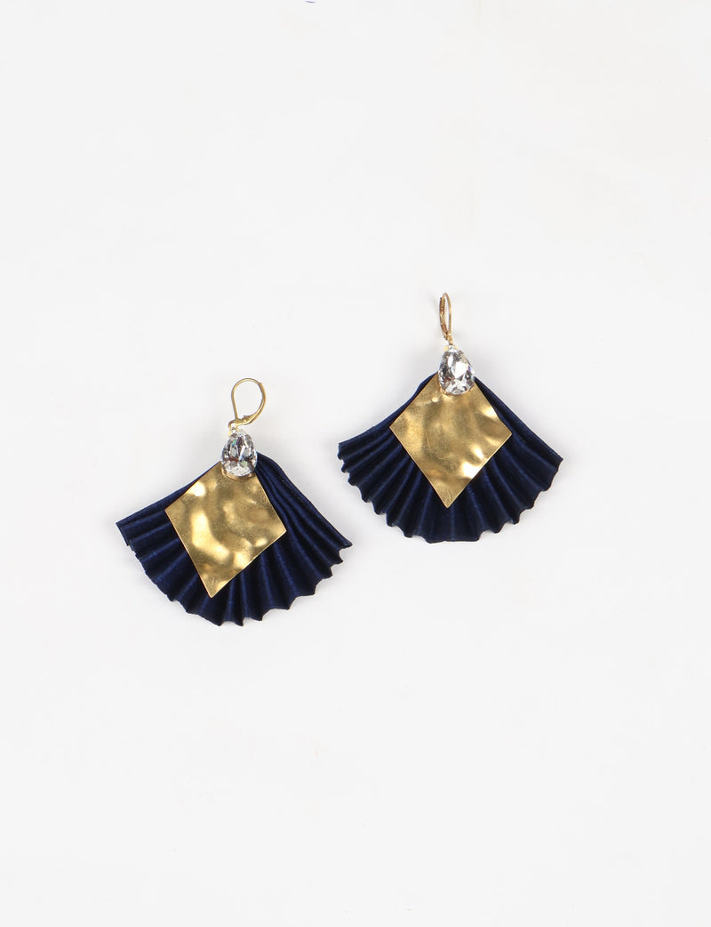 Pair of pleated navy blue earrings with hammered gold diamond-shaped accents and clear teardrop crystals, flat lay view