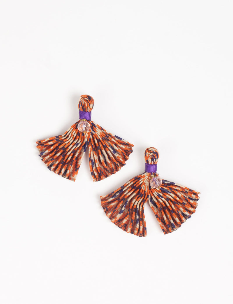 Pair of pleated fabric earrings in beige, orange, and purple abstract pattern with purple band and clear bead, flat lay