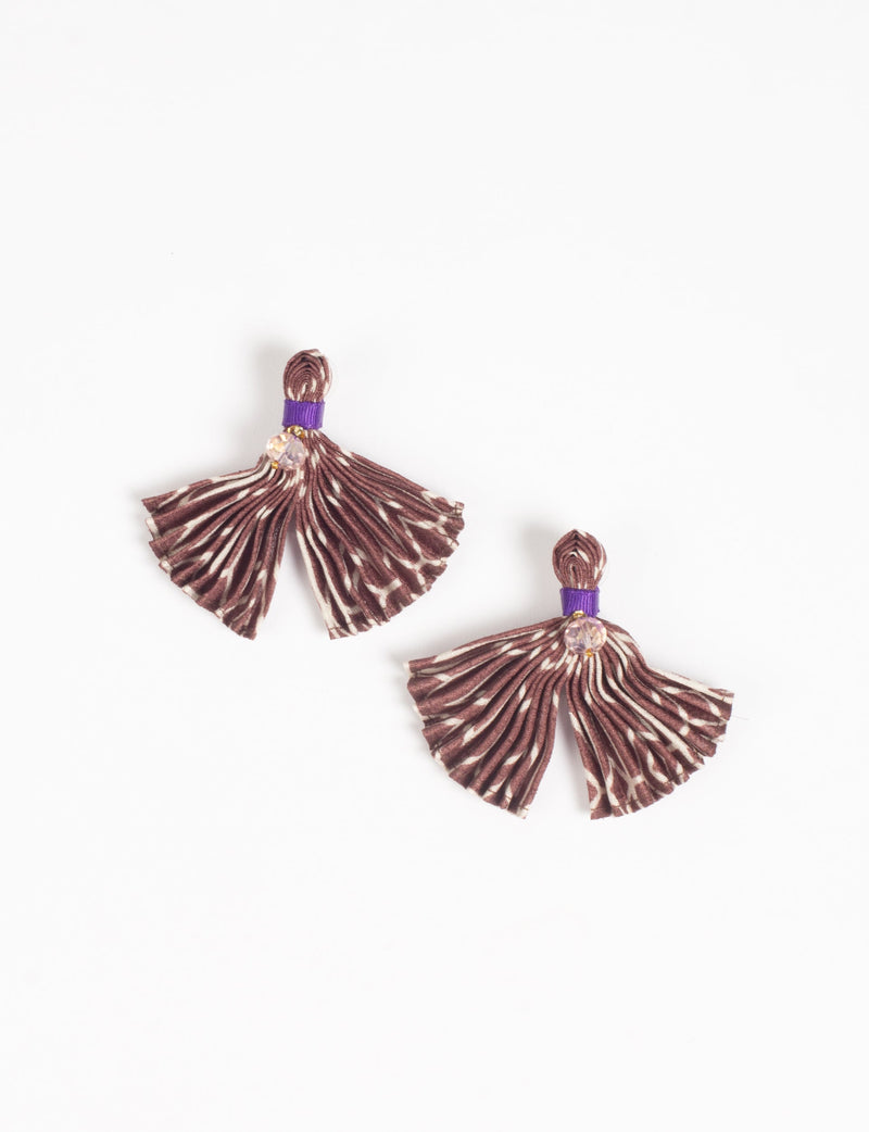 Beige and brown pleated fabric earrings with abstract pattern, purple band, and small clear bead, flat lay on white background