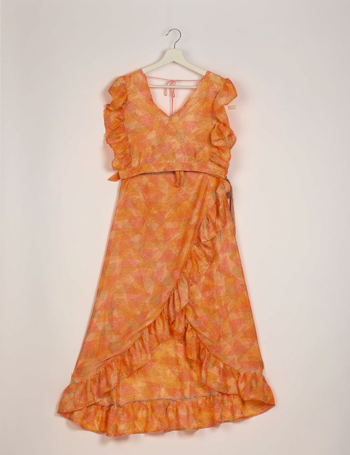 Orange abstract print frill skirt set with V-neck, ruffled sleeves, and wrap-style skirt hanging on white hanger