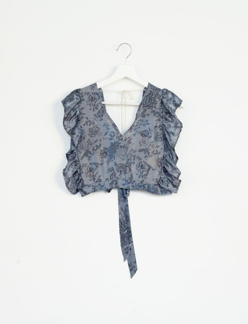 Grey tropical floral print frill sleeve crop top with V-neck and tie detail hanging on white hanger against white background