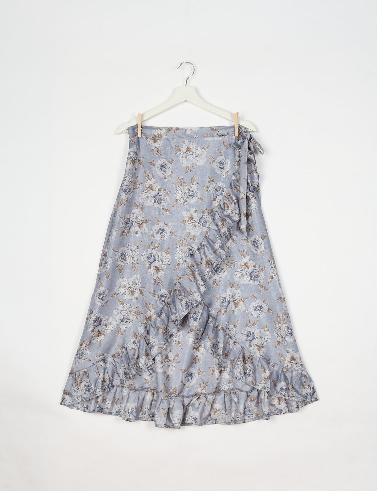 Grey floral wrap skirt with ruffle trim and side tie, hanging on white hanger against white background