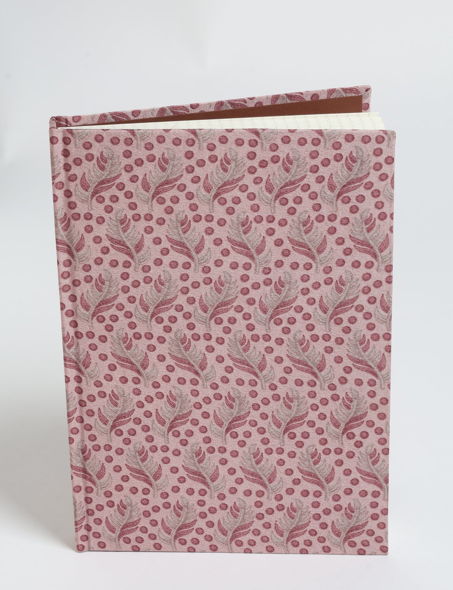 A5 hard cover notebook with pink fabric cover featuring a leaf and dot pattern, shown partially open from a side angle
