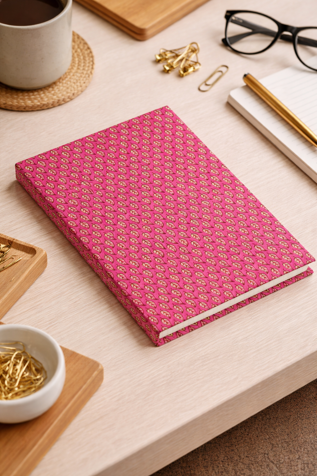 A5 hard cover notebook with pink cover featuring a repeating pattern of small beige leaves, flat on a light wood desk