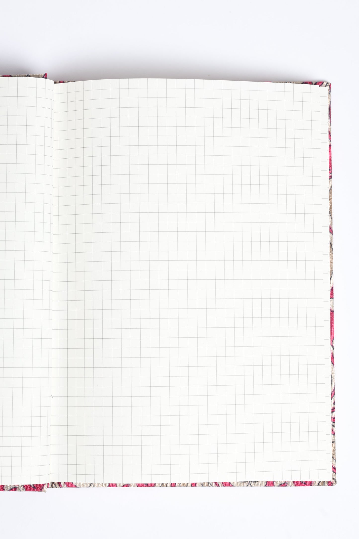 Open A5 hard cover notebook with pink leaf patterned fabric cover and blank grid pages, flat lay view