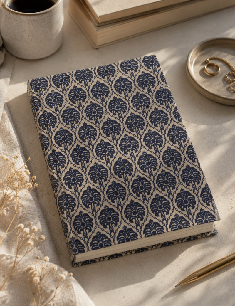 A5 hard cover notebook with blue leaf pattern on beige cover, shown flat on a table with a pen and coffee cup nearby