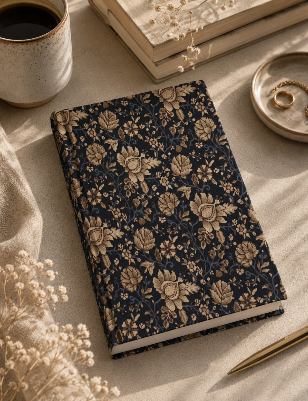 Hardcover notebook with blue cover and beige floral pattern, shown flat on a beige surface with coffee cup and pen nearby